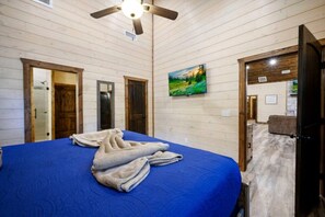 Una stanza con un letto, una ventola a soffitto, pareti in legno, un quadro e una porta che dà su un'altra stanza.