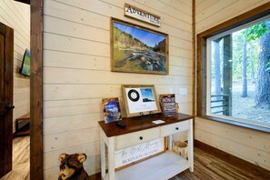 Interior de una cabaña de madera con un escritorio de madera, una fotografía enmarcada de un paisaje, un cartel de bienvenida y un letrero que indica la ubicación como Broken Bow, Oklahoma.