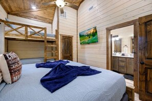 Una habitación de cabaña de madera con literas, un cuadro, un baño con espejo y un ventilador de techo.