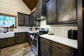 A kitchen with dark wooden cabinets, a stainless steel stove, and a white countertop. - Peaceful Easy Feeling · Woodland Retreat: Hot Tub, Swing Chairs, Fire Pit (Broken Bow)