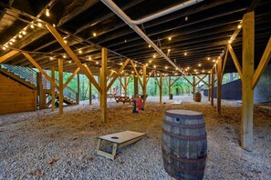 An indoor wooden structure with a gravel floor, wooden beams, and string lights. - Peaceful Easy Feeling · Woodland Retreat: Hot Tub, Swing Chairs, Fire Pit (Broken Bow)