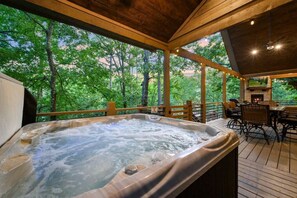A hot tub with a wooden deck and outdoor seating area, surrounded by trees. - Peaceful Easy Feeling · Woodland Retreat: Hot Tub, Swing Chairs, Fire Pit (Broken Bow)