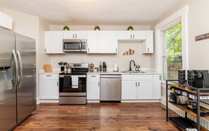 A modern kitchen with stainless steel appliances, white cabinetry, and a wooden floor. - Louisville Charm | 3BR | King Beds | Private Yard (Louisville)