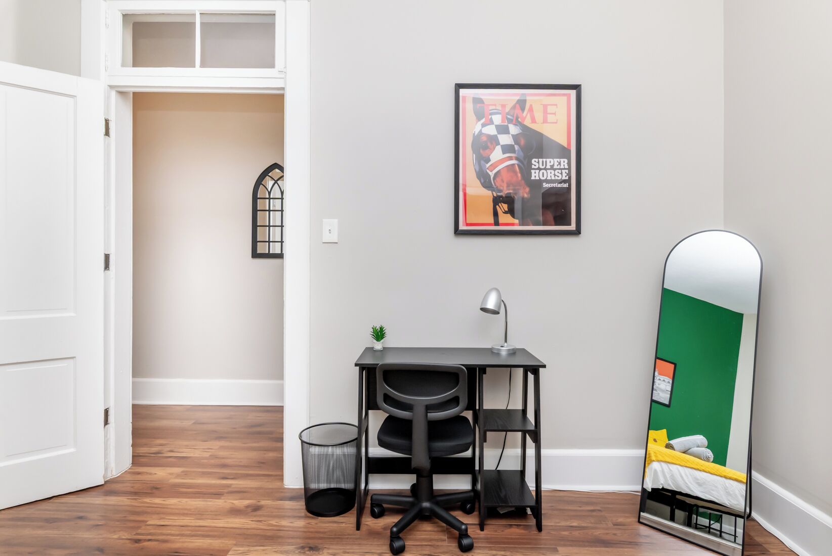 A room with a desk, chair, and a bed with a green wall.