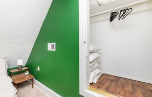 A room with a green wall, a wooden bench with a lamp, a white bed, and a white door with a window. - Louisville Charm | 3BR | King Beds | Private Yard (Louisville)