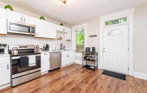 A modern kitchen with stainless steel appliances, white cabinetry, and a wooden floor. - Louisville Charm | 3BR | King Beds | Private Yard (Louisville)
