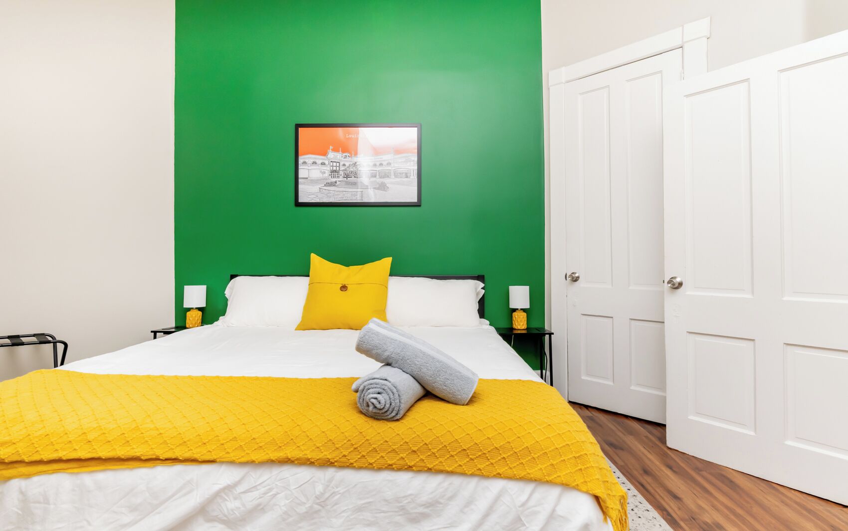 Una habitación de hotel con cama, una pared verde decorativa, un cuadro enmarcado y una puerta blanca.
