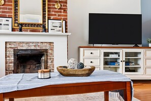 A living room with a brick fireplace, a television, and a wooden cabinet with drawers. - Louisville Charm 5BR Retreat | Expo | Dwntwn (Louisville)
