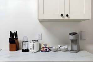 A kitchen with a white countertop, a coffee maker, a toaster, a blender, a knife block, and a box of sugar. - Louisville Charm 5BR Retreat | Expo | Dwntwn (Louisville)