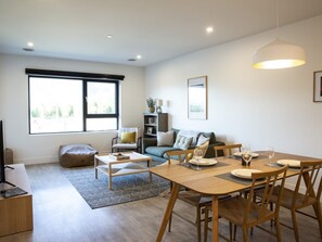 A modern living room with a dining area, large windows, and a sofa. - Revy Mountain Dream (Revelstoke)