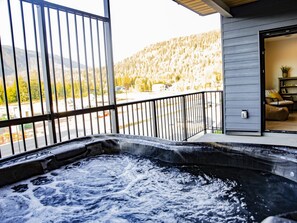 A hot tub on a balcony with a view of a forested mountain. - Revy Mountain Dream (Revelstoke)