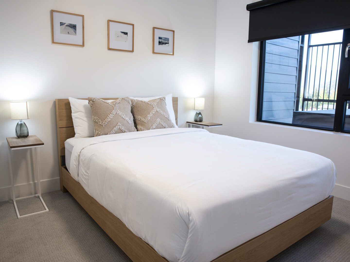 A neatly made bed with a wooden headboard, two bedside tables with lamps, and three framed pictures on the wall.