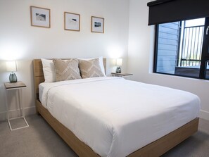 A neatly made bed with a wooden headboard, two bedside tables with lamps, and three framed pictures on the wall. - Revy Mountain Dream (Revelstoke)