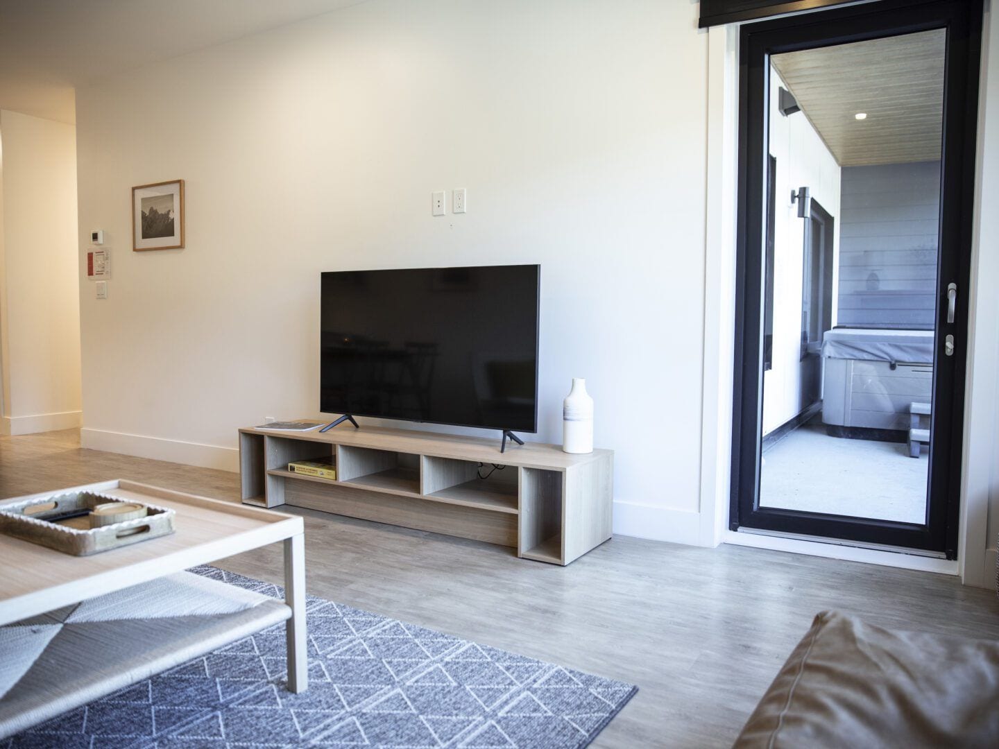 A modern living room with a flat-screen TV on a wooden stand, a coffee table, and a patterned rug.