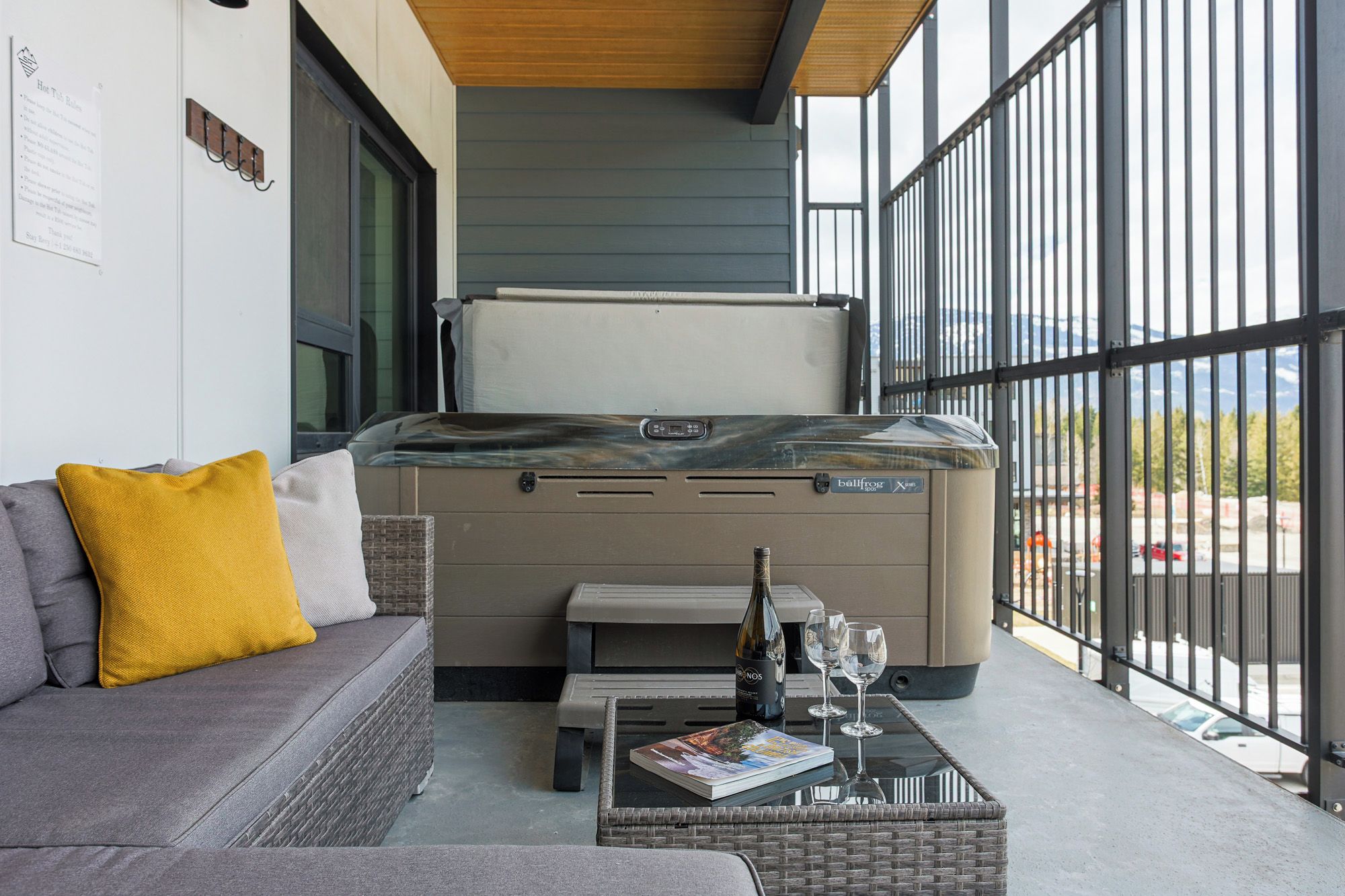 A modern outdoor seating area with a sofa, a table with a magazine, a bottle of wine, and glasses.
