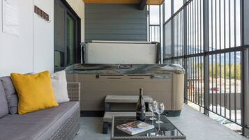 A modern outdoor seating area with a sofa, a table with a magazine, a bottle of wine, and glasses.