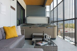 A modern outdoor seating area with a sofa, a table with a magazine, a bottle of wine, and glasses. - Revy Mountain Dream (Revelstoke)