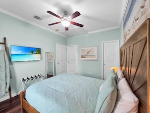 Ein Schlafzimmer mit einem Bett, einem Deckenventilator, einem Fernseher und einem Bild an der Wand.