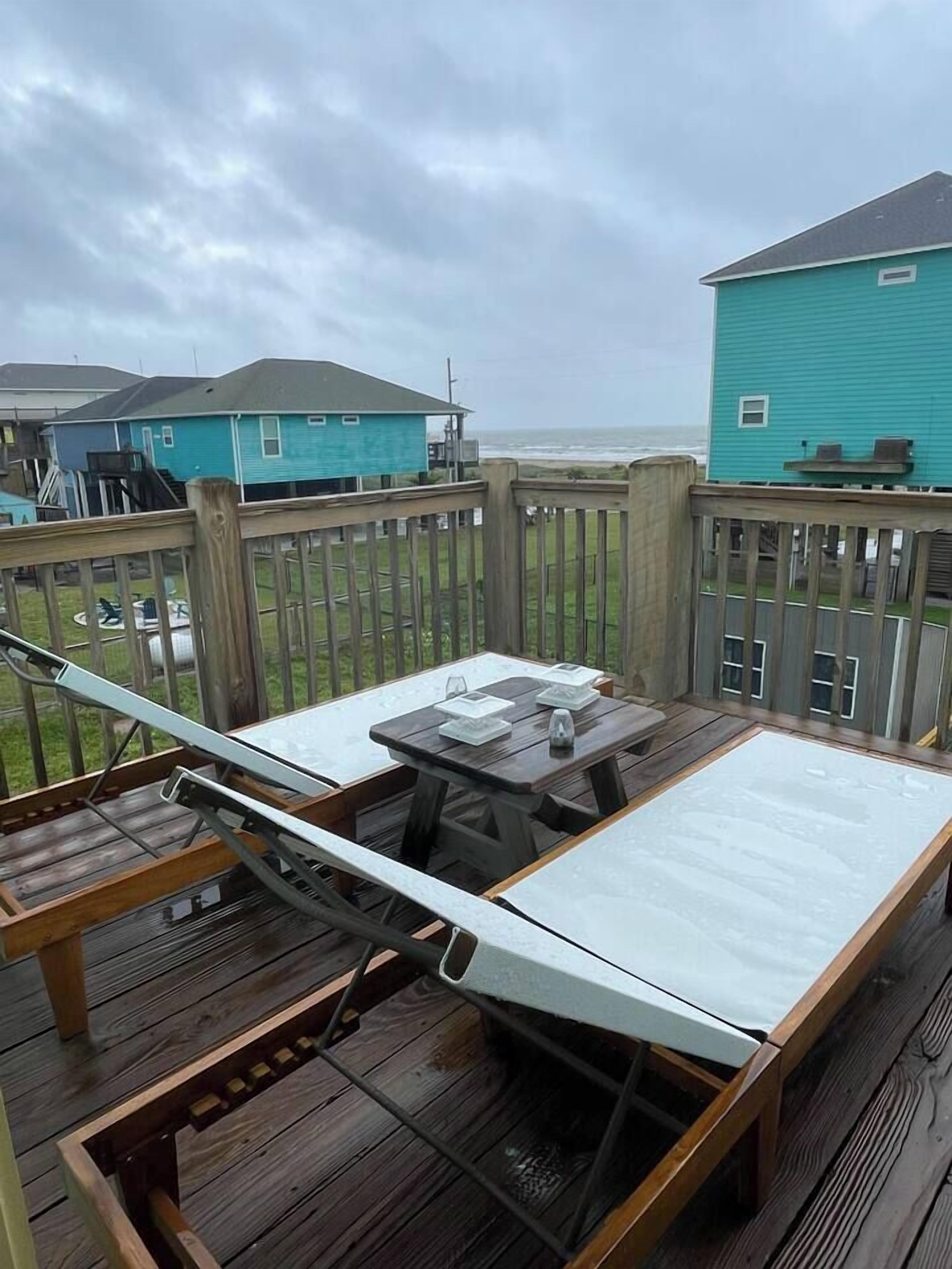 A wooden deck with a table and chairs, overlooking a grassy area and a body of water.