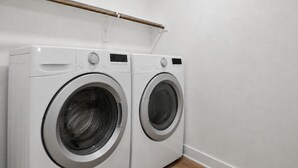 A laundry room with two white front-loading washing machines and a wooden towel rack above them. - New Furnished 3BR 31+ Day Stay Corporate and Family Friendly Garage + Wi-Fi (Fort Worth)