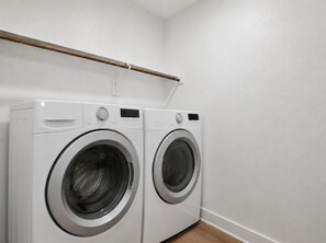 A laundry room with two white front-loading washing machines and a wooden towel rack above them. - New Furnished 3BR 31+ Day Stay Corporate and Family Friendly Garage + Wi-Fi (Fort Worth)