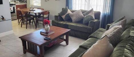 A living room with a green sofa, a wooden coffee table, and a dining area with a table and chairs.