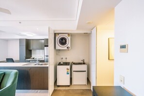 Ein kompaktes Hotelzimmer mit Küchenzeile, darunter eine Waschmaschine, ein kleiner Kühlschrank und ein Spülbecken.