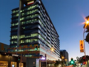 Ein mehrstöckiges Hotel mit modernem Design, das einen markanten Eingangsbereich und ein gut sichtbares Parkschild hat.