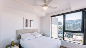 A modern bedroom with a large window, a bed, a bedside table, and a ceiling fan. - Modern Two Bedroom Escape in Fortitude Valley (Fortitude Valley)