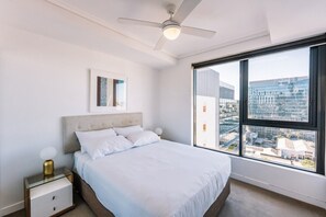 Ein modernes Schlafzimmer mit großem Fenster, einem Bett, einem Nachttisch und einem Deckenventilator.