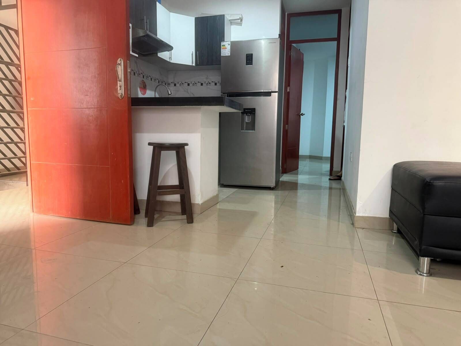 A kitchen with a stainless steel refrigerator, a wooden stool, and a black sofa in a living area.