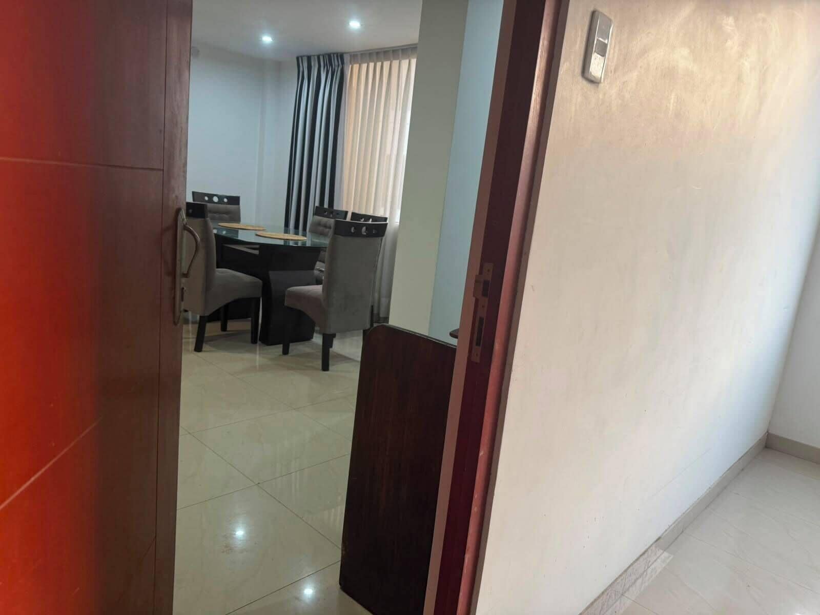A room with a dining table and chairs, a door, and a light switch on the wall.