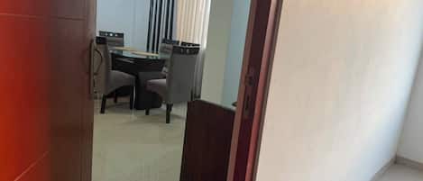 Una habitación con una mesa de comedor y sillas, una puerta e interruptor de luz en la pared.