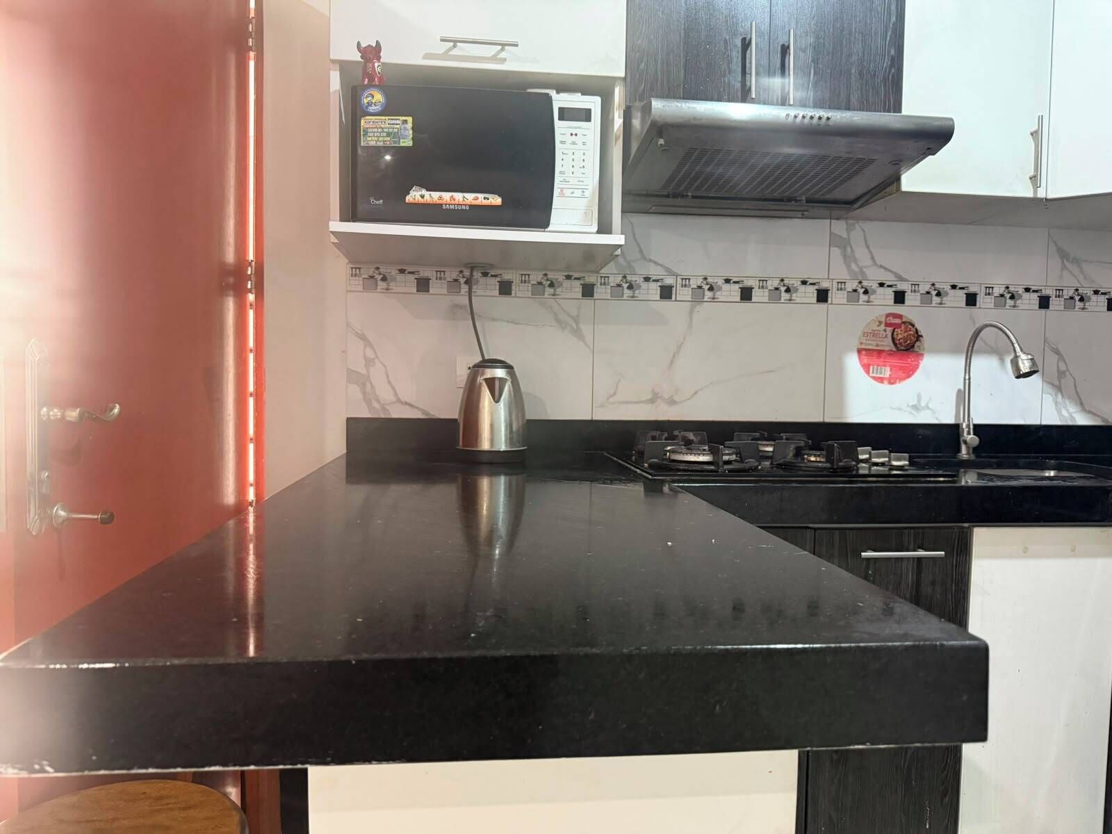 Una cocina con microondas, estufa y hervidor sobre la encimera.