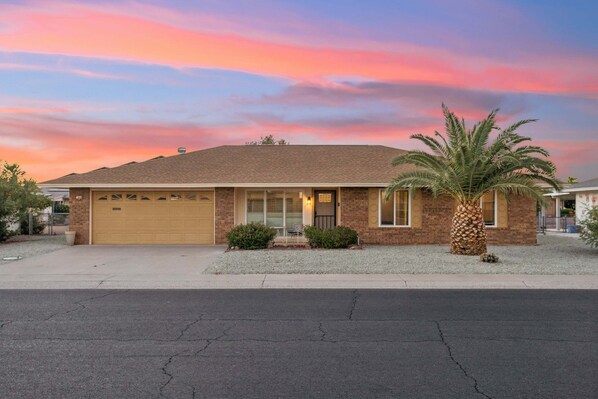 A single-story house with a garage, a small front porch, and a palm tree. - Rolling Hills Haven | 3BR | Large Screened Patio | Fenced Yard | Sun City | Sleeps 6 (Sun City)