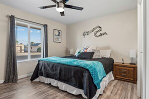 A bedroom with a bed, a nightstand, a ceiling fan, a window with curtains, and a wall with a musical note decoration. - Rolling Hills Haven | 3BR | Large Screened Patio | Fenced Yard | Sun City | Sleeps 6 (Sun City)