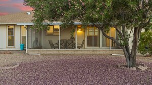 Ein Haus mit überdachter Terrasse, einem Tisch und Stühlen sowie einem Baum im Vordergrund.