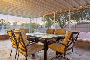 A covered patio with a table and chairs, large windows, and a view of the outdoors. - Rolling Hills Haven | 3BR | Large Screened Patio | Fenced Yard | Sun City | Sleeps 6 (Sun City)
