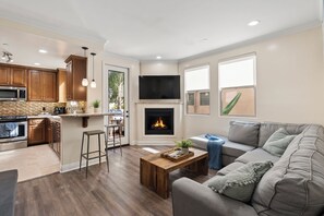 A modern living room with a fireplace, a grey sofa, and a kitchen area with wooden cabinets and a microwave.