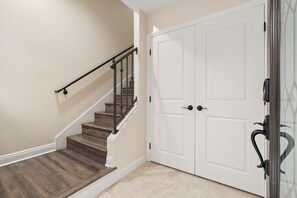Una escalera con barandilla que lleva a una plataforma, una puerta blanca con picaporte y una pared con textura.