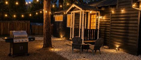 Una cabaña de troncos con un porche, asientos al aire libre y luces colgantes.