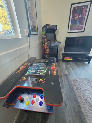 Eine Spielhalle mit einer Mortal Kombat Maschine, einer Maschine mit Spiderman-Motto und einem Fernseher im Hintergrund.