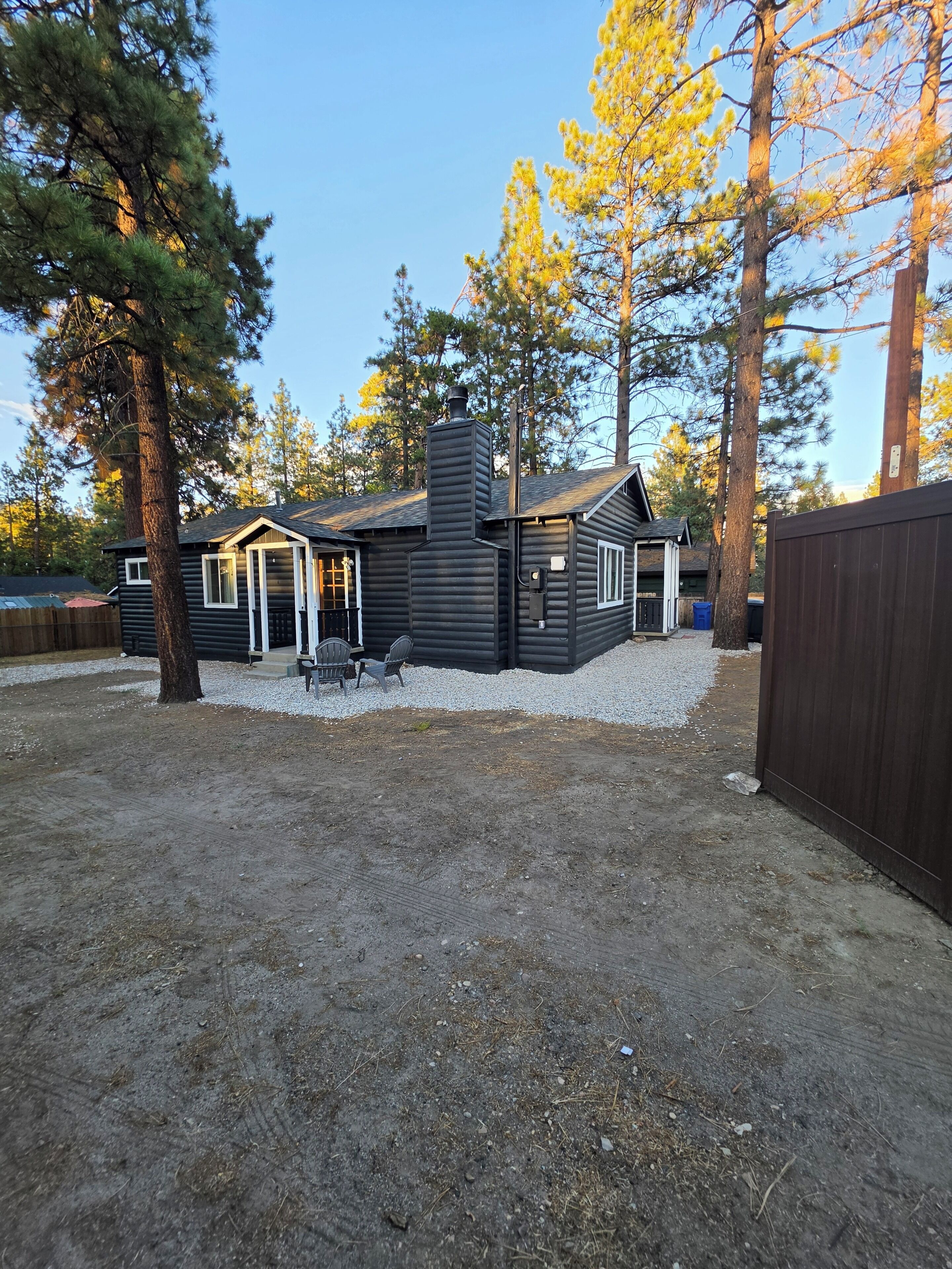 A cabin with a chimney, a deck with chairs, and a fenced yard.