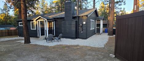 A cabin with a chimney, a deck with chairs, and a fenced yard.