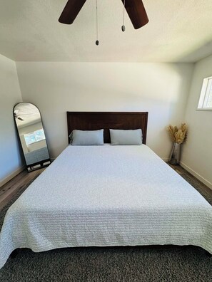 A bedroom with a large bed, a wooden headboard, a ceiling fan, and a mirror on the wall. - Cozy Big Bear Cabin _Game Room-Pet Friendly- Near Lake-Sleeps 8 (Big Bear)