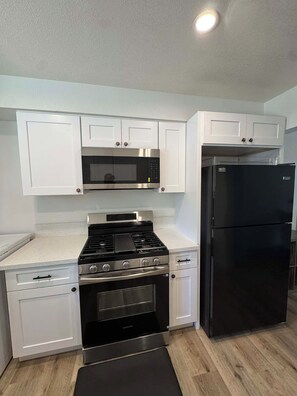 A kitchen with white cabinets, a black stove, a black refrigerator, and a microwave. - Cozy Big Bear Cabin _Game Room-Pet Friendly- Near Lake-Sleeps 8 (Big Bear)