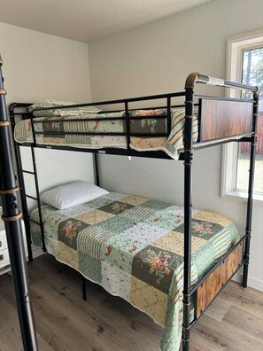 Ein Stockbett mit einer gesteppten Bettdecke und einem Fenster zur Rechten.