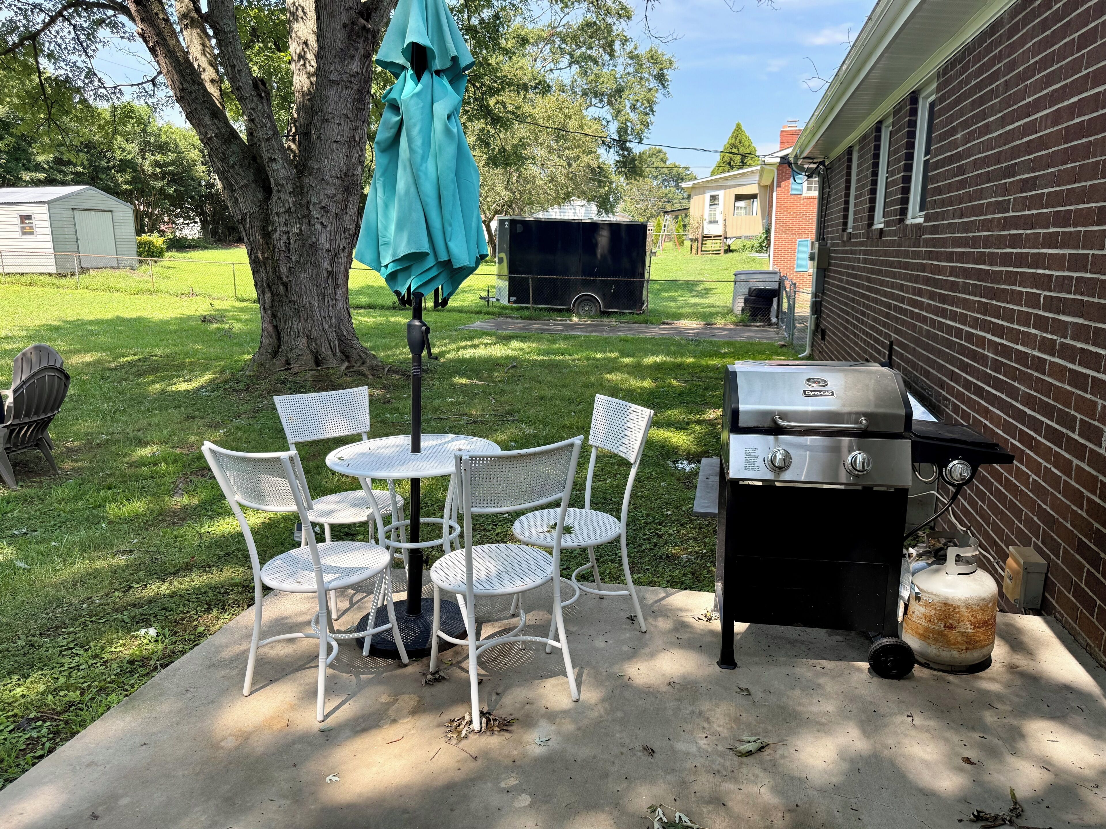 An outdoor patio with a table and chairs, a grill, and a covered umbrella.
