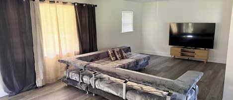 A living room with a sectional sofa, a flat-screen TV, and a wooden entertainment unit.