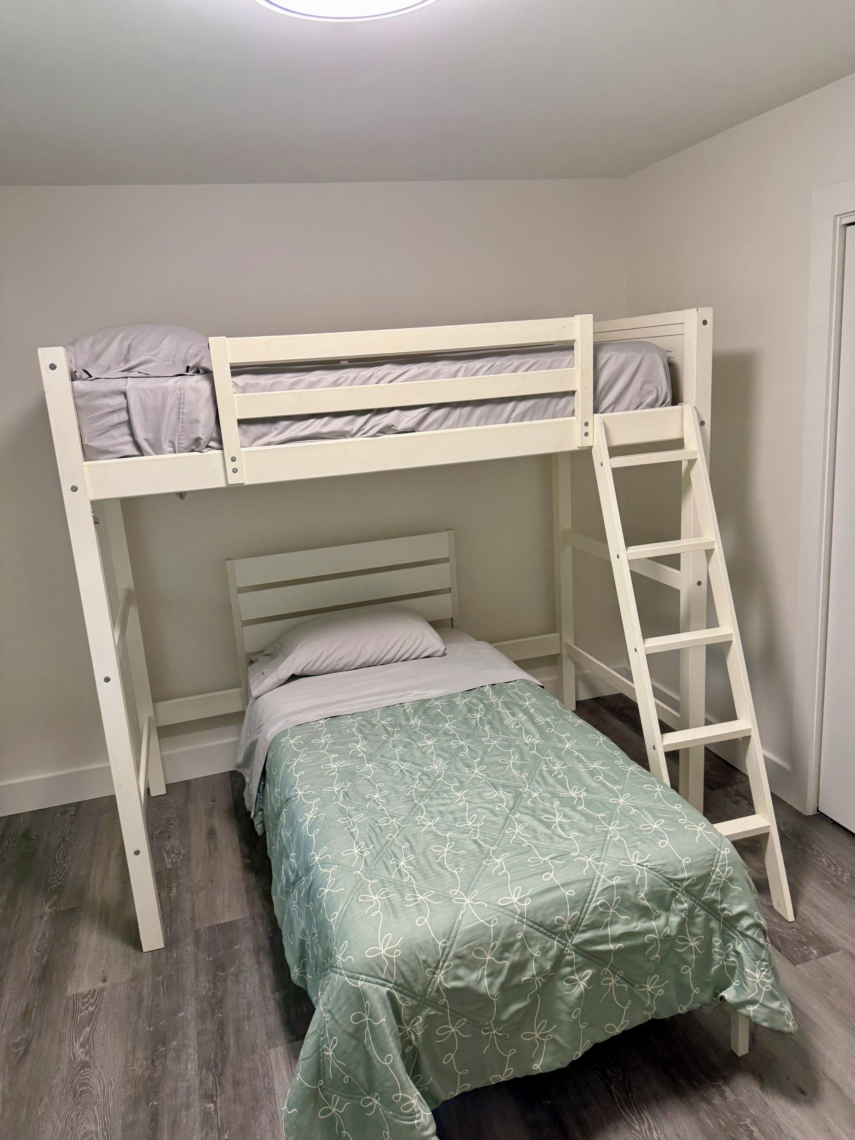 A bunk bed with a ladder, a single bed below, and a patterned bedspread.